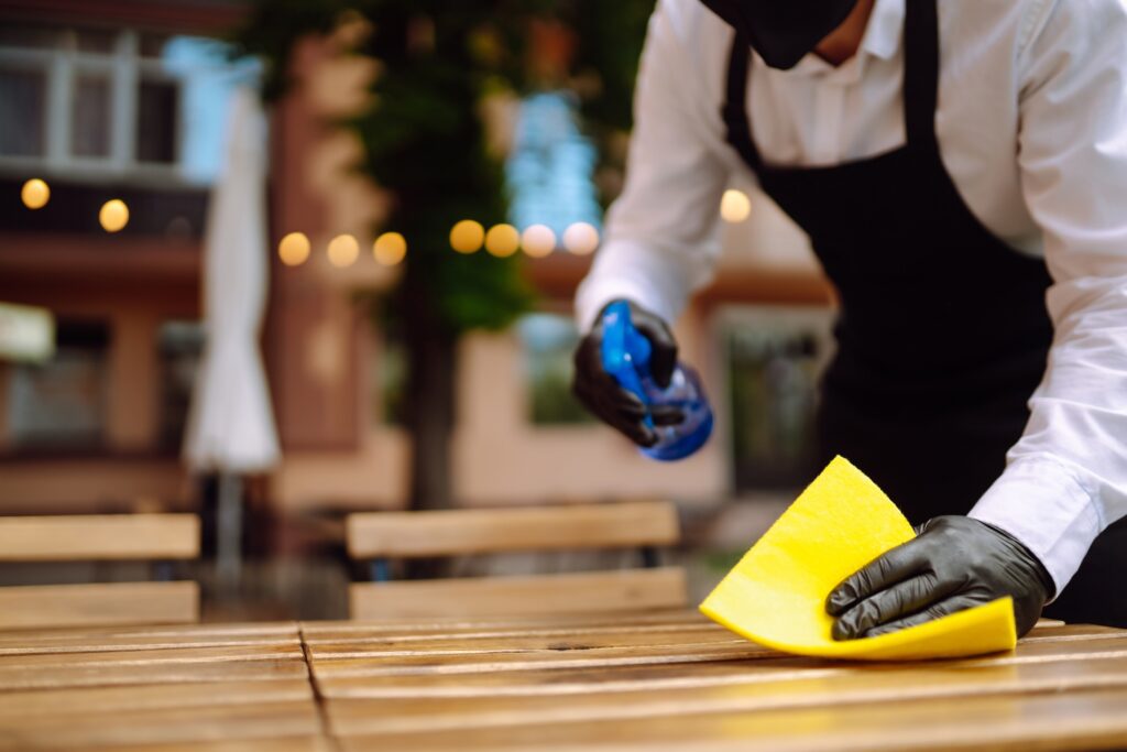 a man from a commercial cleaning company sprays and disinfects a table at an event venue for a golf tournament in phoenix